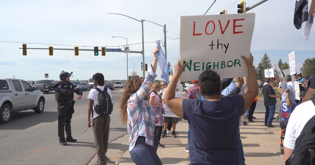 A protest with a person holding a sign that says "Love thy neighbor"