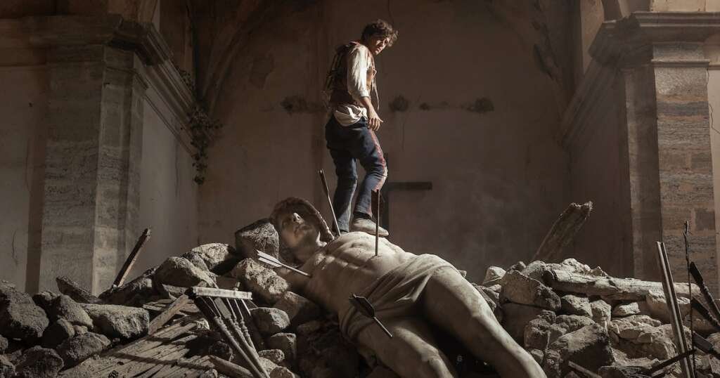 A man stands on a statue in a scene from La Bola Negra