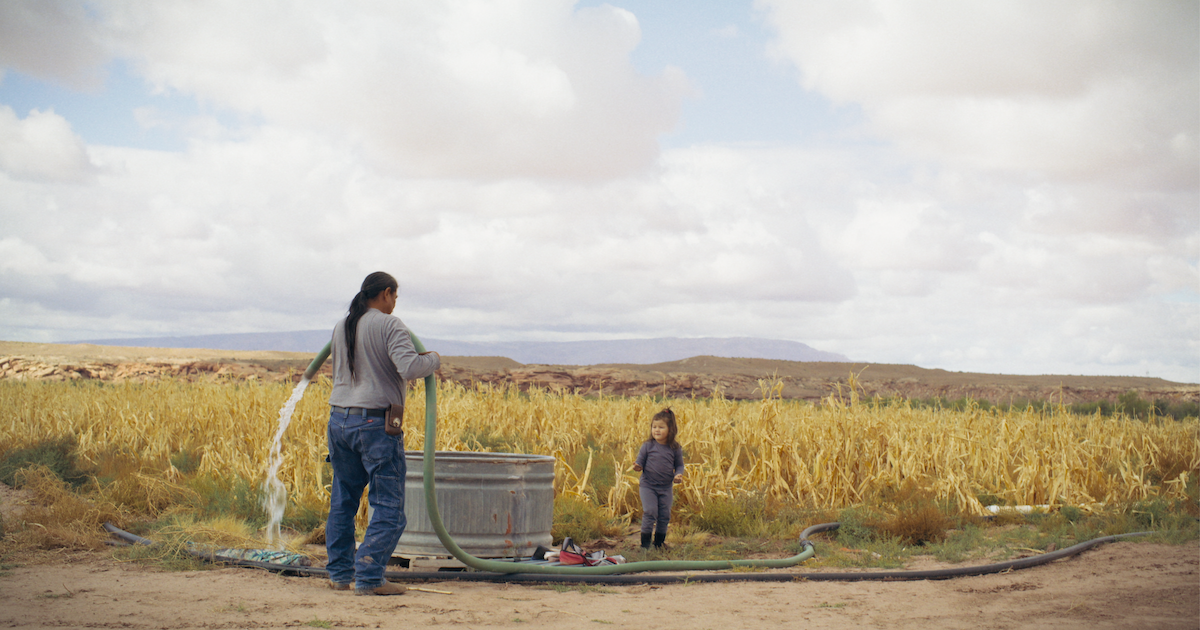 Two people stand in nature watering plants during a scene from "The River"