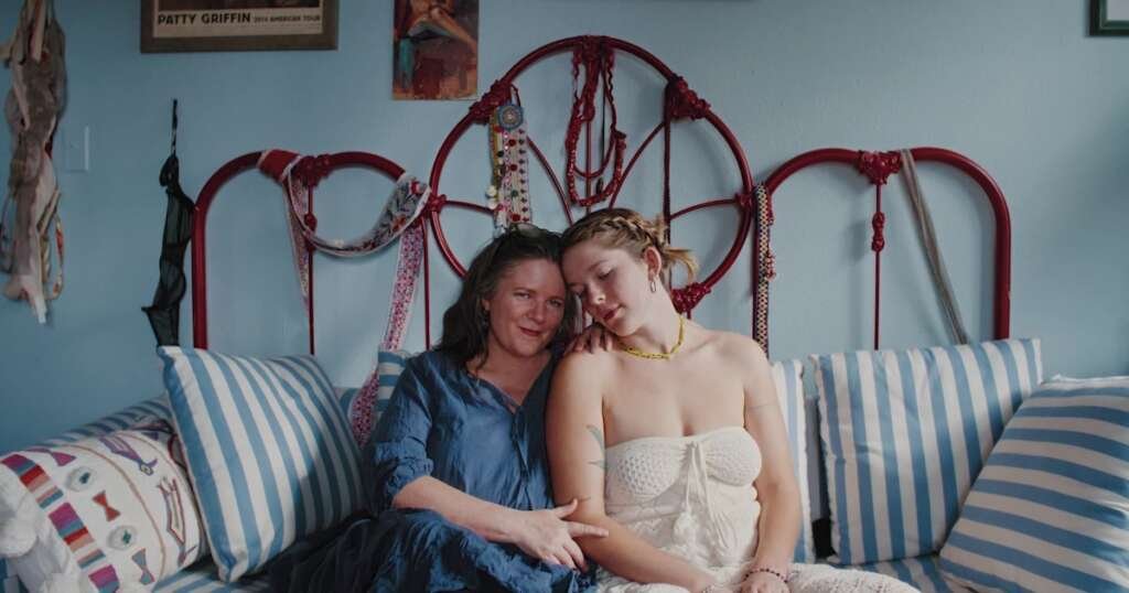 A mother and daughter sit together on a bed in "Watch You Rise."